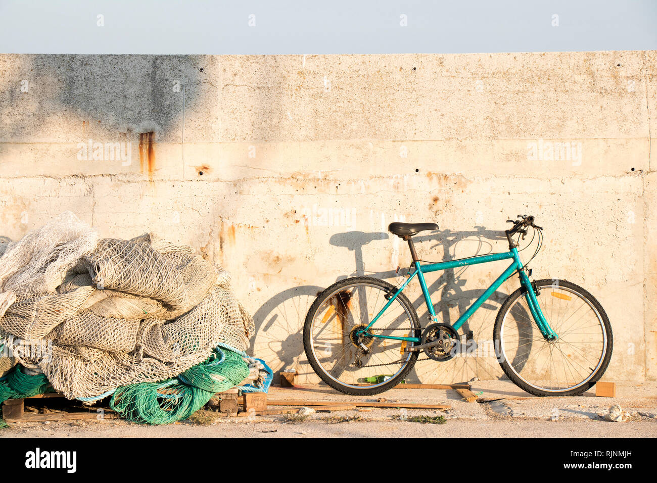 Montón de viejas redes de pesca de arrastre erosionados y una bicicleta estacionada en la aldea de pescadores del muelle en un día soleado Foto de stock