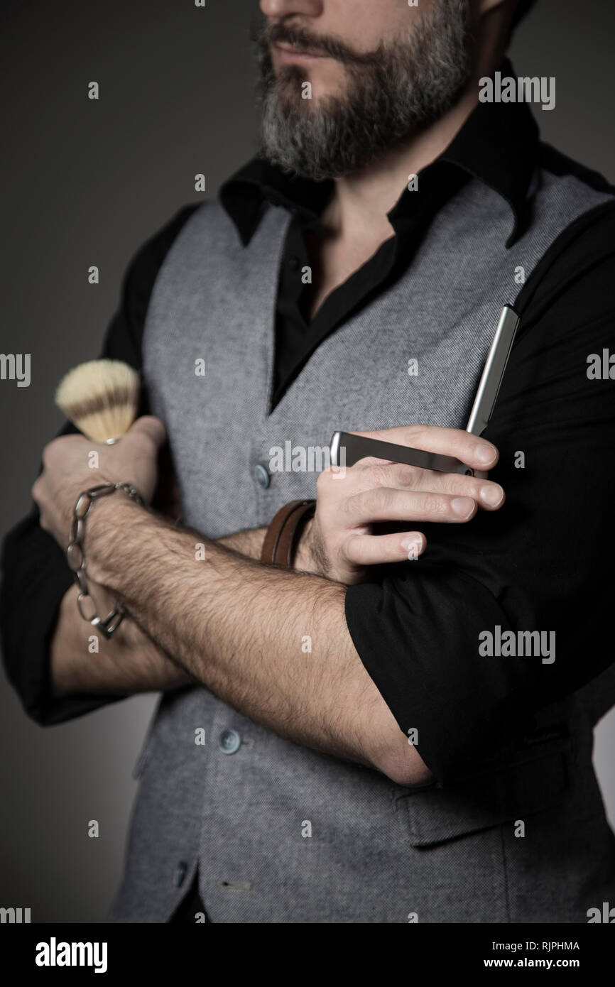 Retrato de un peluquero de moda con una camisa negra y un chaleco holding  afeitado clásico herramientas en sus manos Fotografía de stock - Alamy