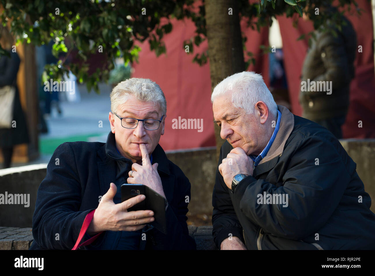Italia, Lombardía, Monza, los ancianos en el banquillo estudiar cómo funciona un teléfono móvil Foto de stock