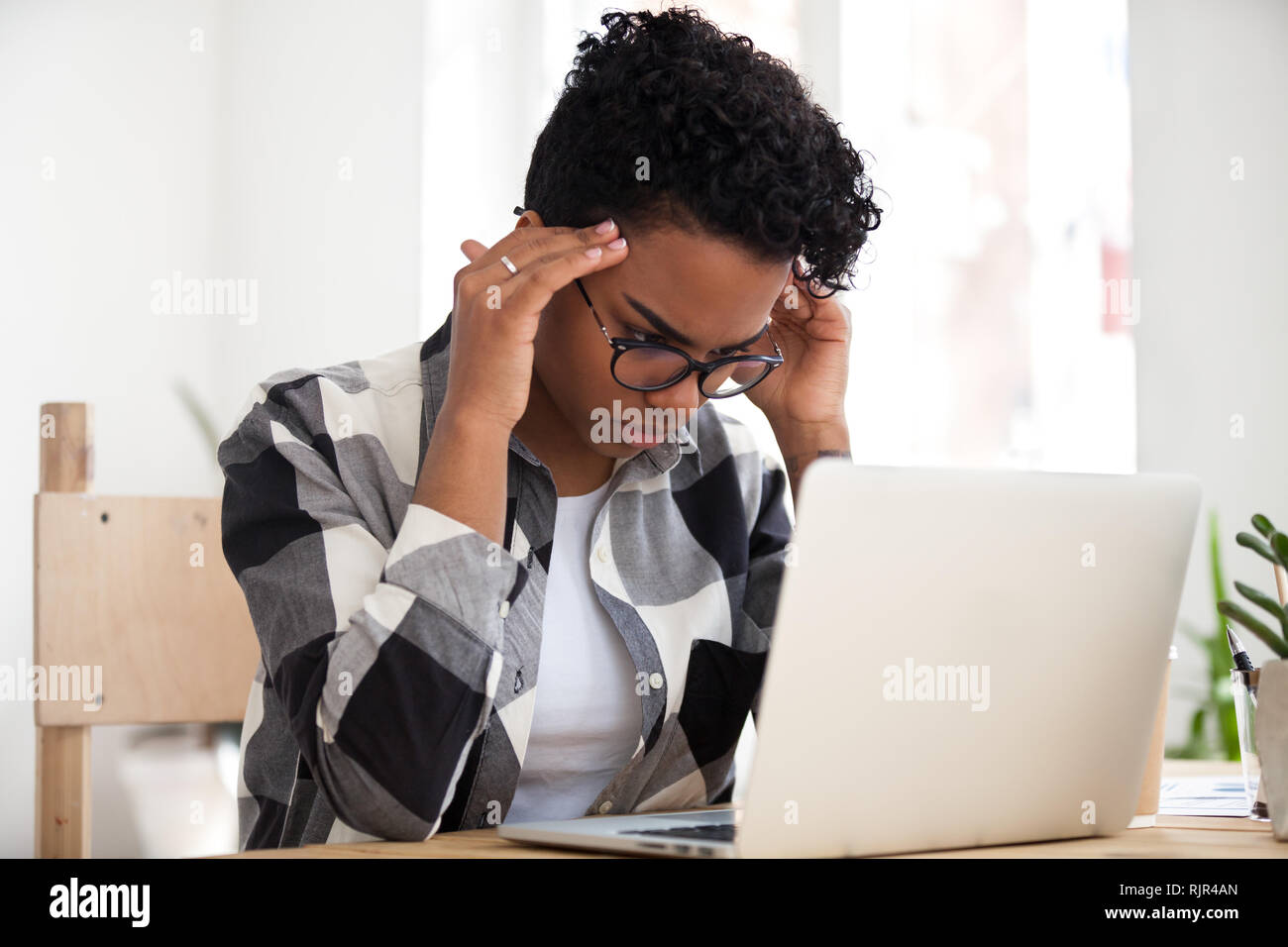 Subrayó mujer africana concentrando haciendo difícil trabajar con el ordenador en línea Foto de stock