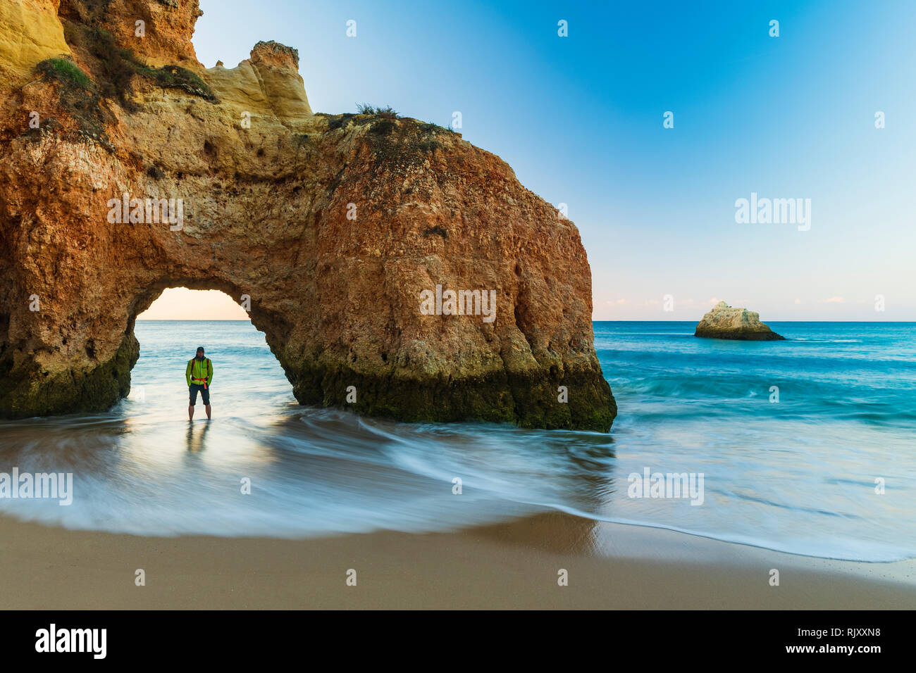 Hombre de pie debajo del arco natural del acantilado, mirando la vista de mar, Alvor, Algarve, Portugal, Europa Foto de stock