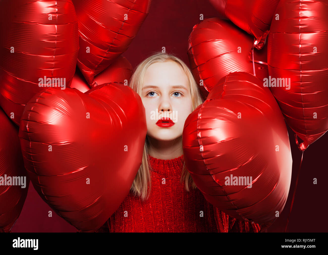 Joven hermosa jovencita buscando corazón rojo sobre fondo de globos Foto de stock