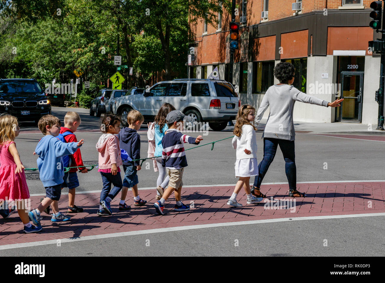 Adulto, posiblemente profesor principal niños cruzando la calle con una cuerda. Foto de stock