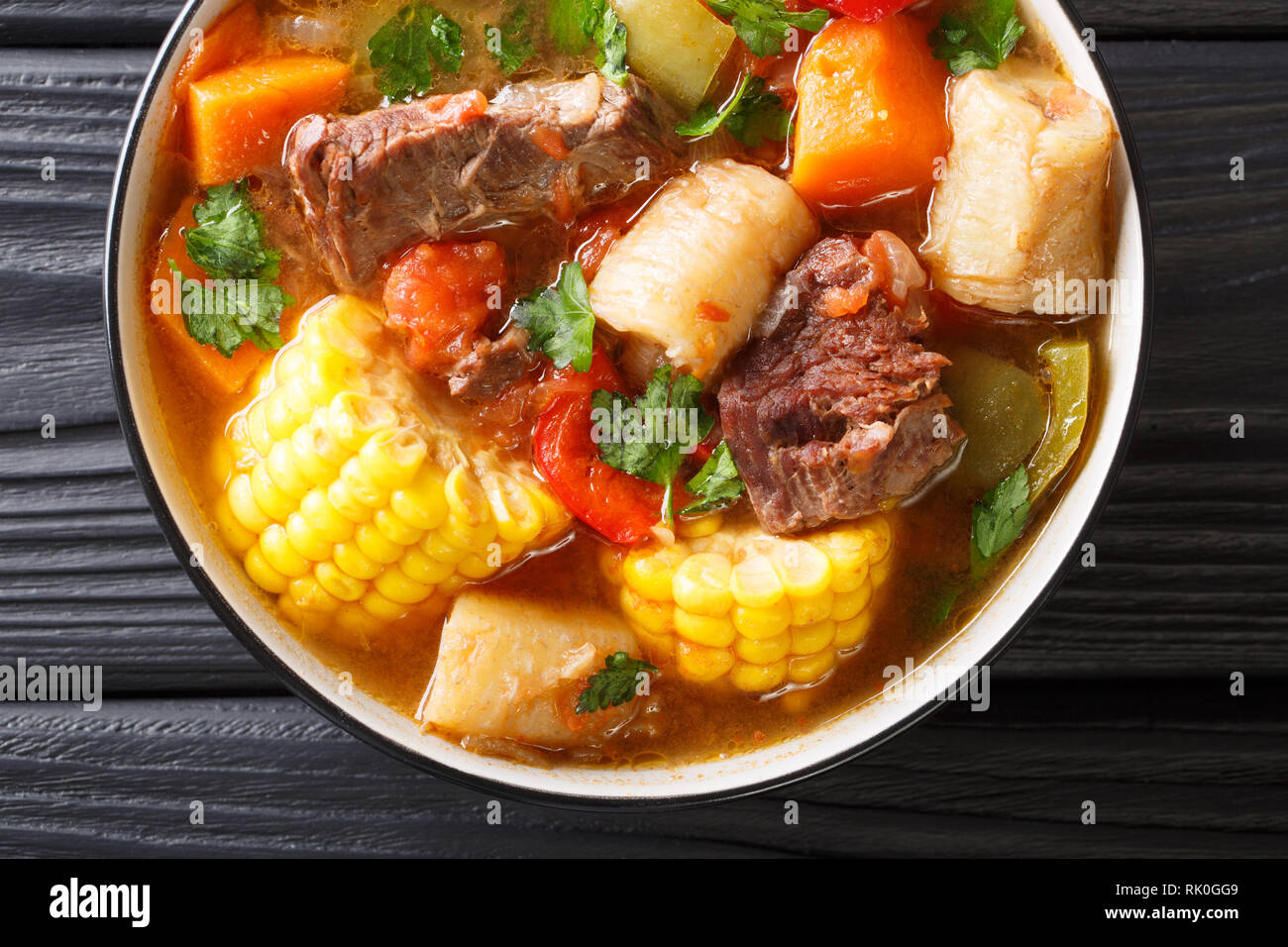 Sancocho Latinoamericano espesa sopa de carne con verduras de cerca en un plato sobre la mesa. Vista superior horizontal desde arriba, estilo rústico Foto de stock