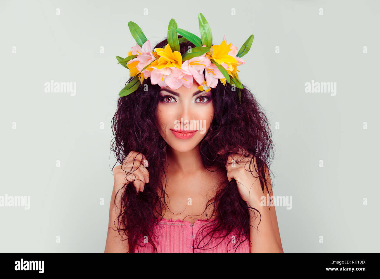 Mujer atractiva celebración tocando su pelo rizado con ambas manos.  Mestizos hispano latina colombiana modelo en corona de flores en la cabeza,  una morena rizado h Fotografía de stock - Alamy
