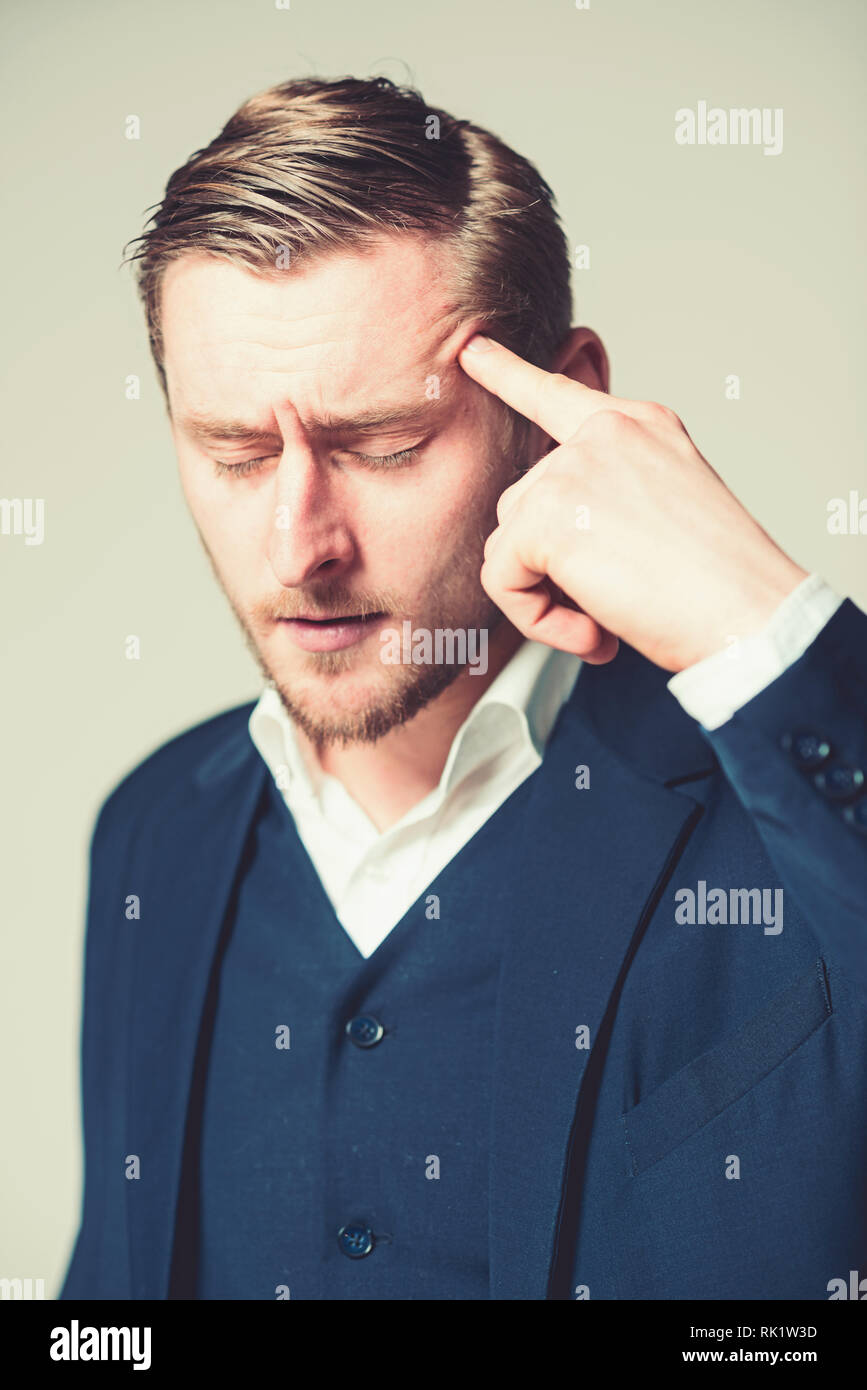 Joven intelectual con los ojos cerrados tratando con problemas con el retrato del hombre de negocios cansados presionando su dedo índice en la cabeza aislada sobre gris Foto de stock