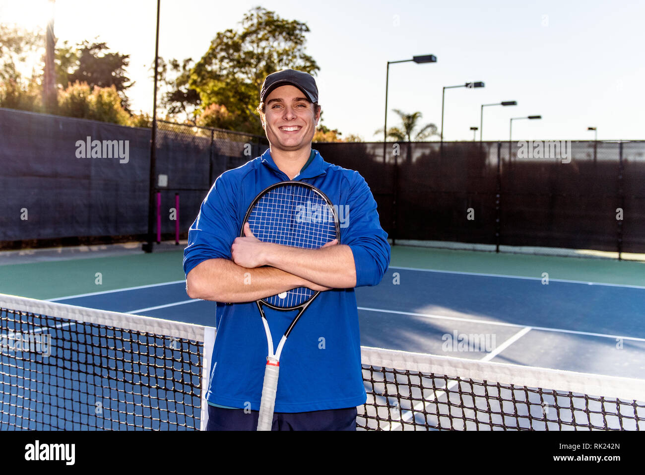 Joven y de buena apariencia de tenis profesional docente mostrando la sonrisa y la expresión feliz en la cancha de tenis. Foto de stock