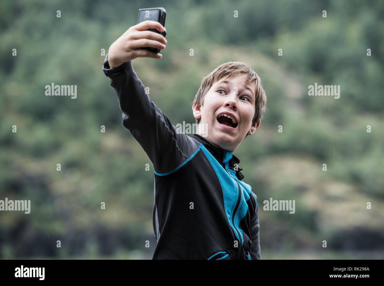 Cándido retrato de joven teniendo selfie usando el teléfono móvil, el bosque en el fondo, cerrar Foto de stock