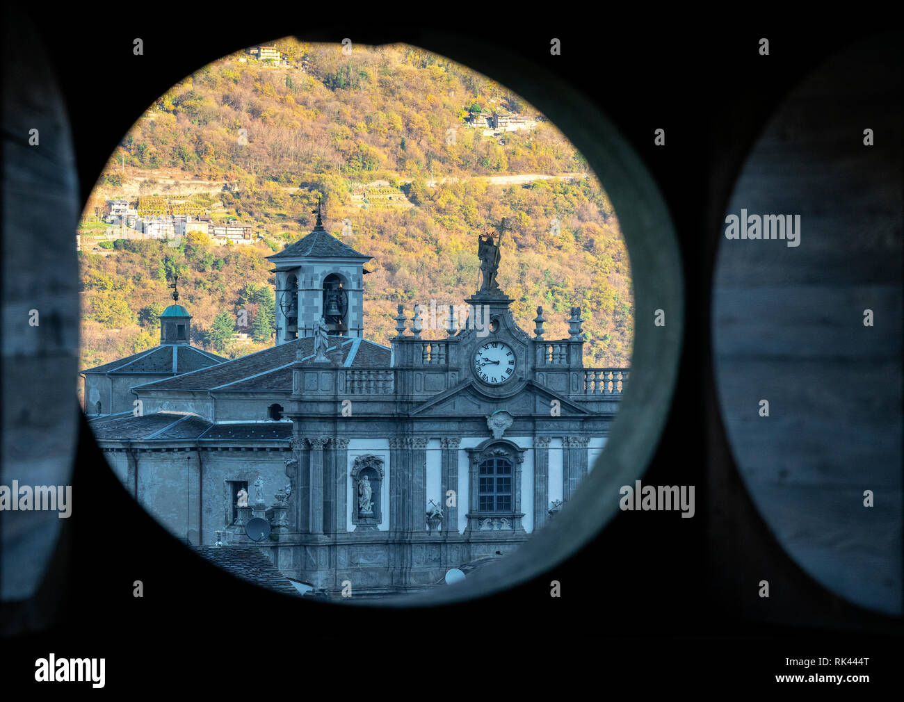 Vista de la fachada barroca de la iglesia románica de Collegiata di San Giovanni Battista de apertura a través de un orificio circular en el interior del Palazzo Malacrida, Morbegno Foto de stock