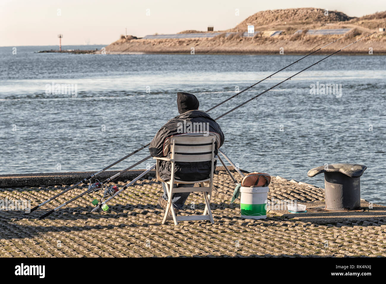 El pescador se encuentra en el lado del canal en una silla de