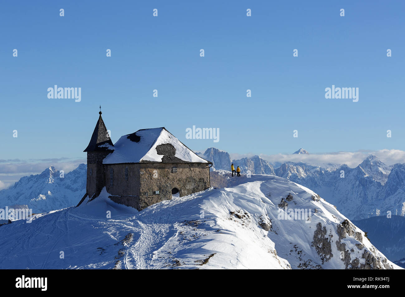 Madre e hijo de pie junto a una hermosa iglesia cubierto de nieve con una vista impresionante sobre las montañas, Dobratsch, Austria Foto de stock