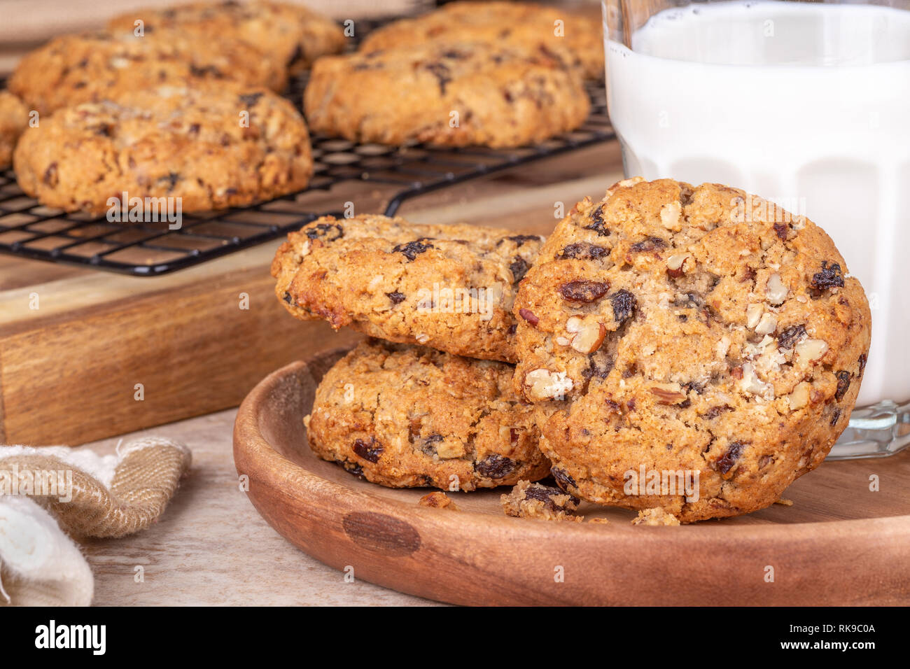 Primer plano de avena tuerca pasas galletas y un vaso de leche con galletas en un rack de refrigeración en segundo plano. Foto de stock