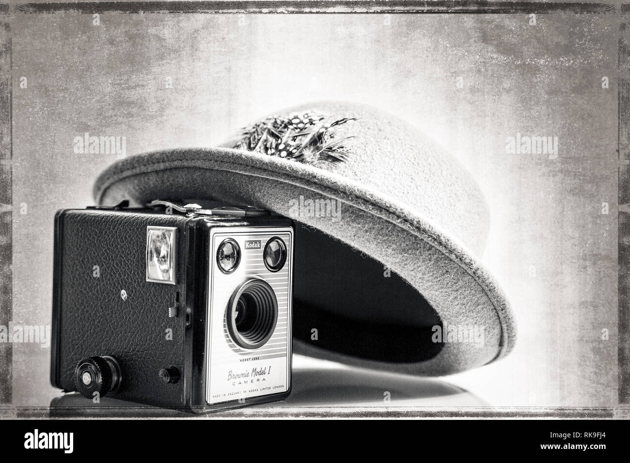 Black & White de cerca de 1950 sombrero Fedora artísticamente inclinada en vintage Caja cámara Kodak Brownie (modelo 1) del mismo período. Efecto de edad antecedentes. Foto de stock
