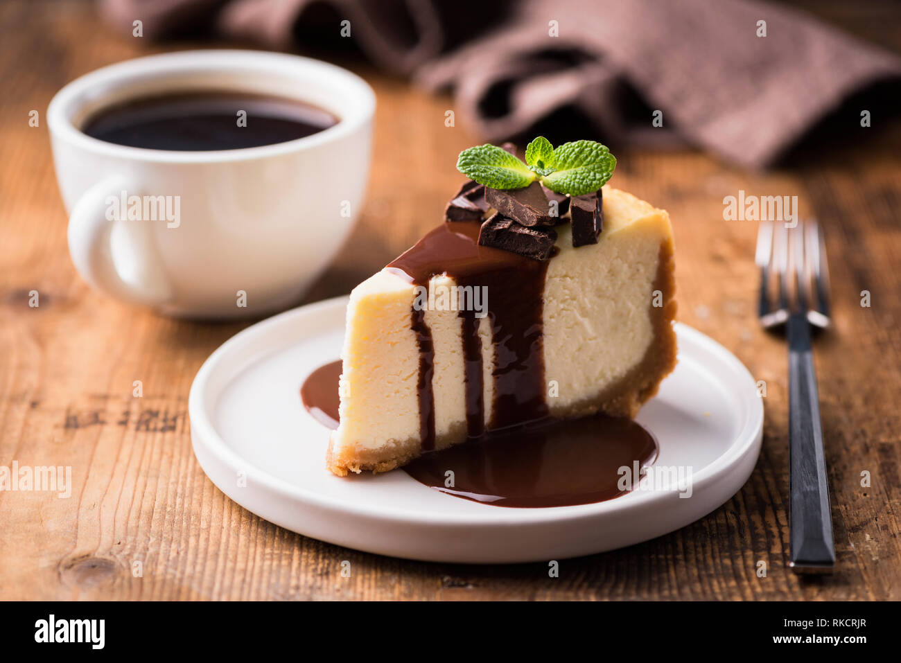 Cheesecake con salsa de chocolate y una taza de café negro sobre una mesa de madera. Sabroso aperitivo o café con rebanada de pastel Foto de stock