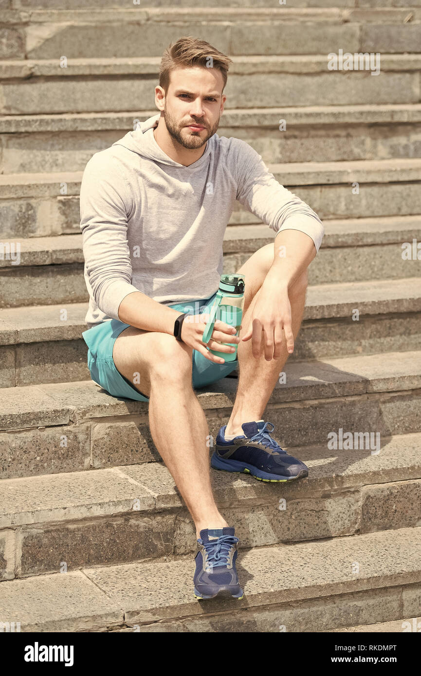 Trabajar en las escaleras. Hombre Apariencia Atlética sostiene la botella  de agua. Atleta hombre ropa deportiva refrescante. Concepto de deporte y  vida sana. Atleta beba agua capacitación en stadium día soleado Fotografía