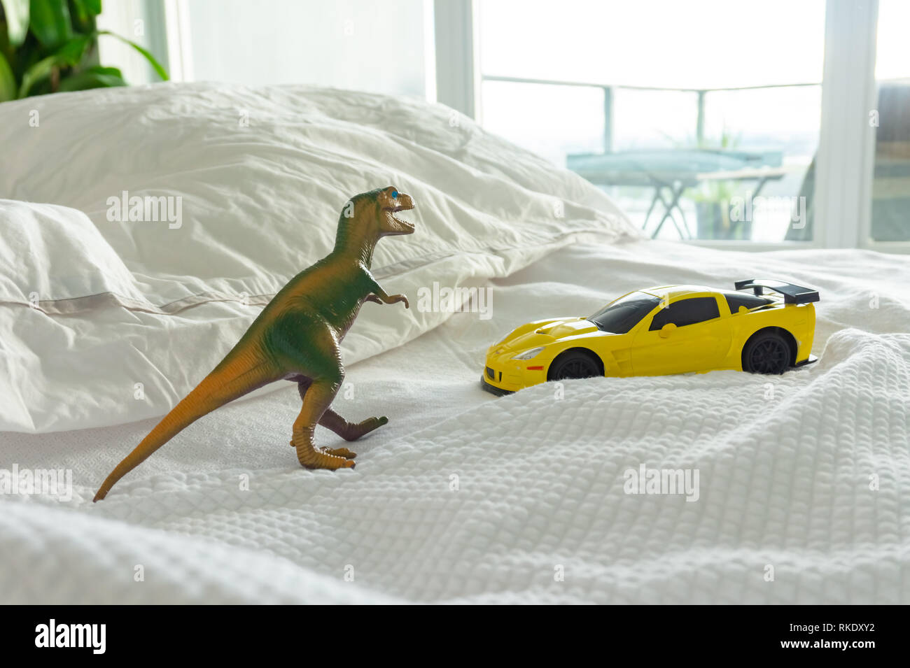 Dinosaurio de juguete y coche en la cama con sus padres, representando el hogar familiar y la crianza de la vida. Sábanas blancas en el fondo. Foto de stock