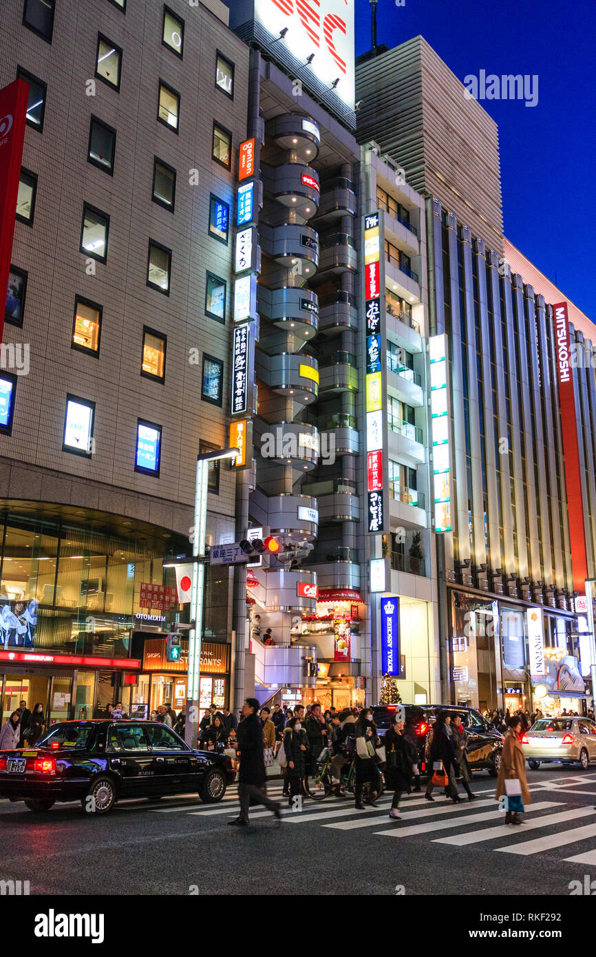 Tokyo, Ginza, noche. La gente que cruza la calle de peatones por el Ibiza tienda con columna de semicírculo, balcones y Royal Asscher store Foto de stock