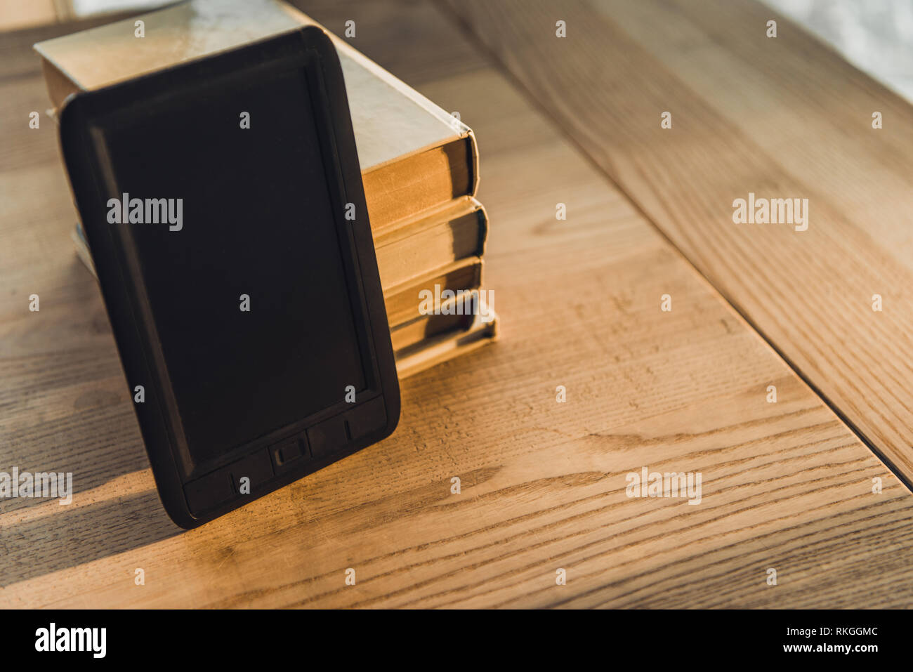 E-reader con pantalla en blanco cerca de los libros de papel sobre la mesa de madera Foto de stock