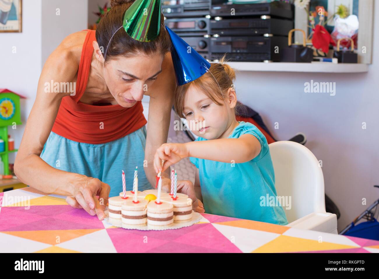 Tres años el niño y la mujer rubia con cono de color tapas, en la fiesta de  cumpleaños, poner velas en la tarta con forma de flor en coloridos manteles  en Fotografía
