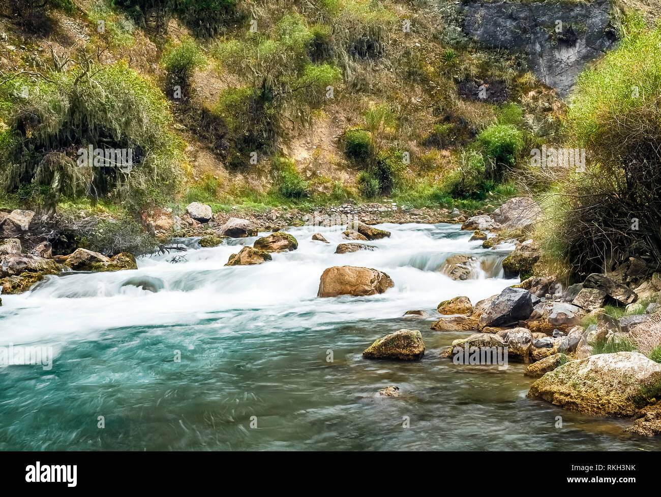 Exposición larga vista escénica de un río turquesa suavizadas en los andes peruanos con rocas en primer plano y vegetaciones en los lados Foto de stock