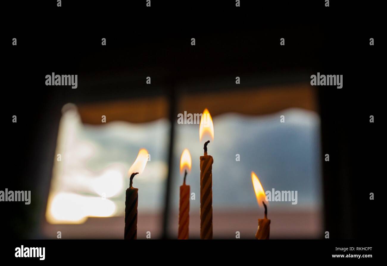 Cuatro velas de cumpleaños en la parte superior de un Pastel oscuro sobre fondo de cielo azul de la ventana. Closeup. Foto de stock