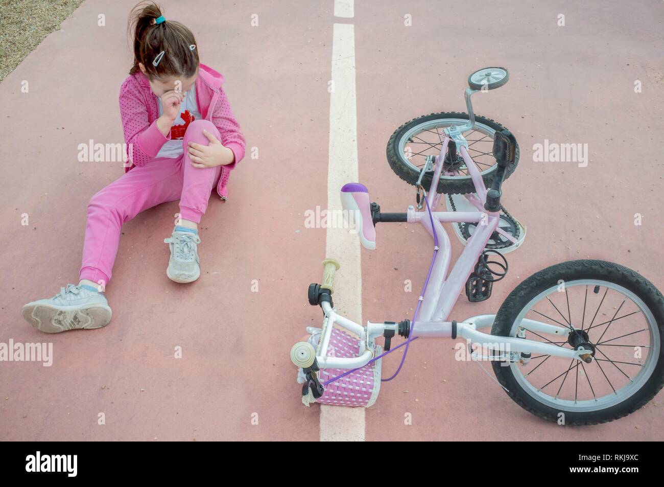 Niño Niña llorando después del accidente de bicicleta. Hembra de color rosa en el piso en bicicleta con ruedas de entrenamiento. Foto de stock