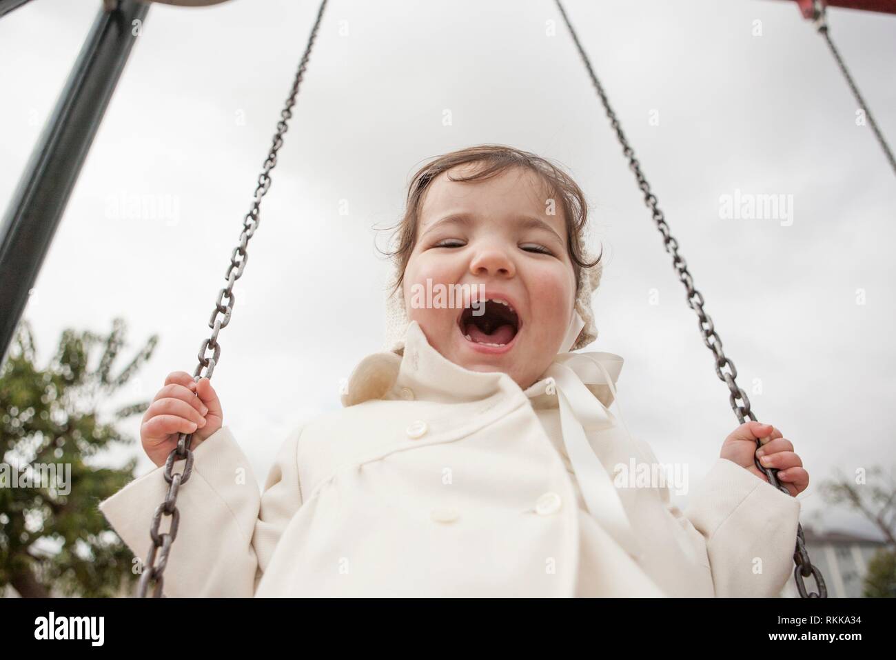 Feliz 2 años de edad, niña divirtiéndose en un columpio en invierno. El enfoque selectivo. Foto de stock