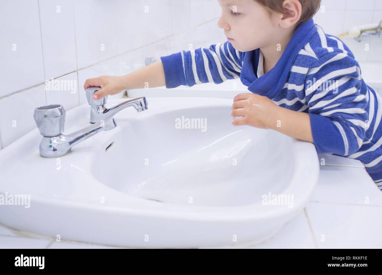 Niño de 3 años el lavado de manos en el lavabo escolar adaptado. El aprendizaje de hábitos de higiene. Foto de stock