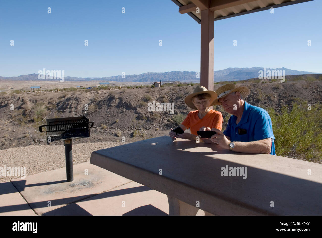 Pareja mayor caucásica (de 60 a 70 años) revisando las fotos de los teléfonos celulares mientras se relaja en Lake Mead Recreation Area, Nevada, Estados Unidos. Foto de stock