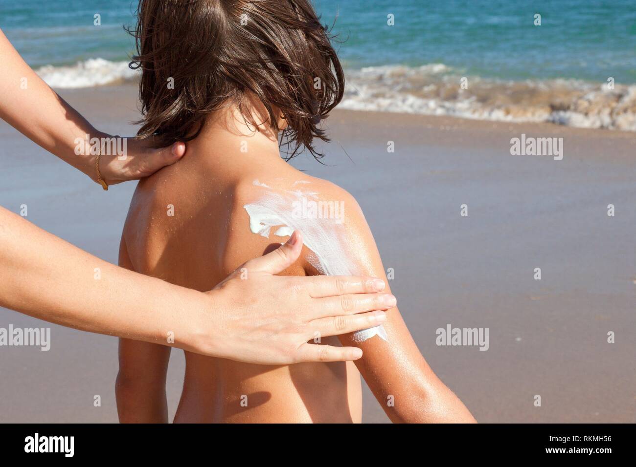 Madre aplicar bloqueador solar crema a su hija en un brazo. Idílica playa de fondo. Foto de stock