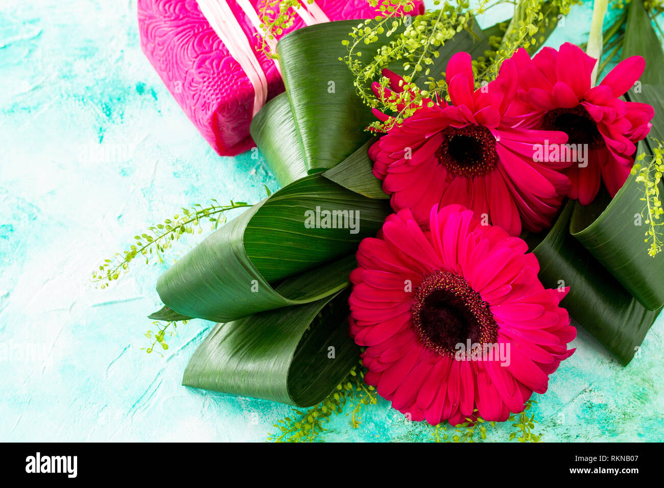 Día de la Madre Día del fondo o tarjeta de felicitación. Bouquet de gerberas  Flores Rojas y un presente en una mesa de piedra turquesa. Copie el espacio  Fotografía de stock -