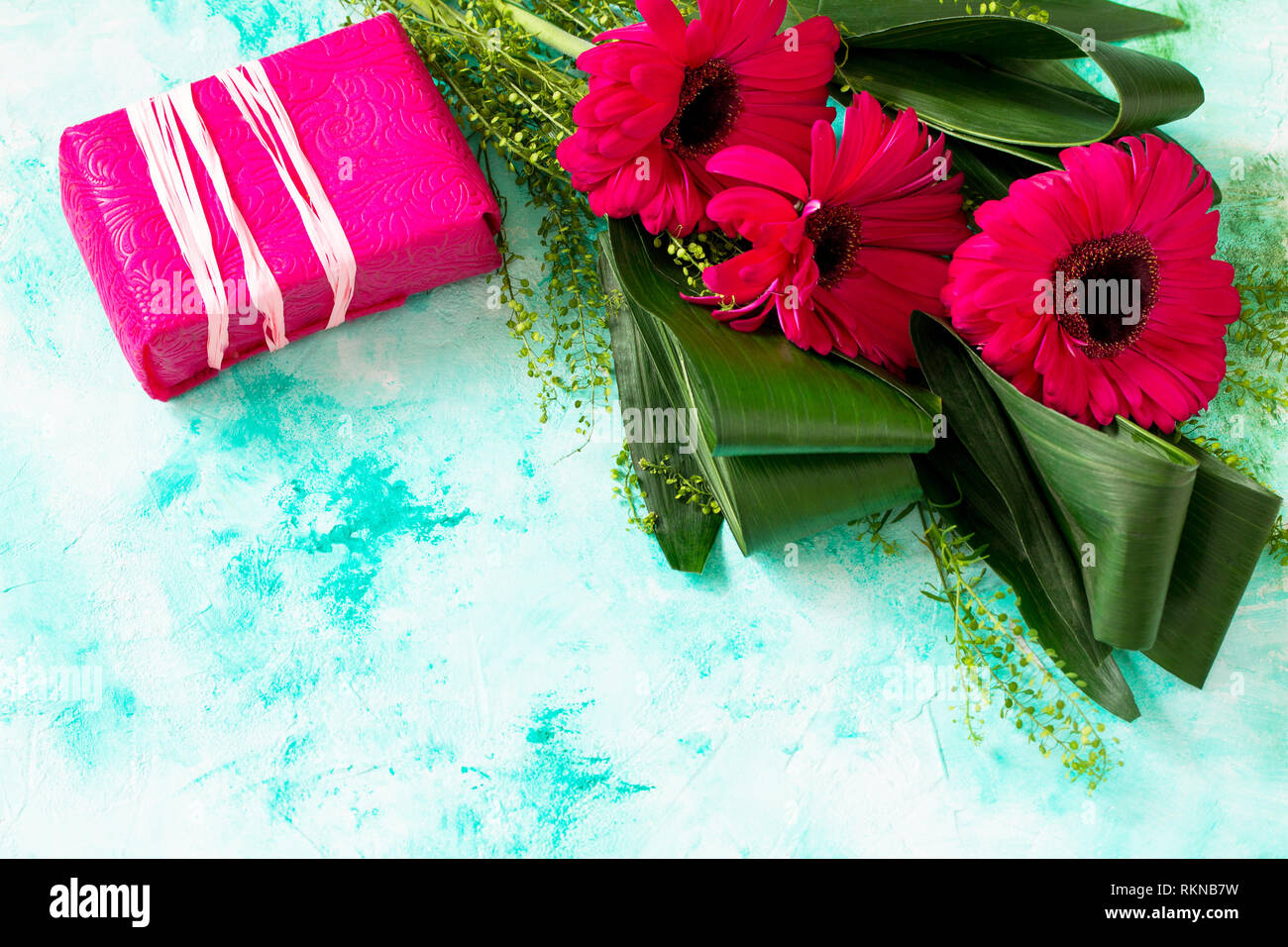 Día de la Madre Día del fondo o tarjeta de felicitación. Bouquet de gerberas  Flores Rojas y un presente en una mesa de piedra turquesa. Copie el espacio  Fotografía de stock -