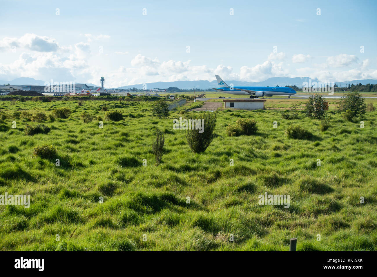 Césped verde y exuberante vegetación que rodea las pistas de aeropuerto como KLM Boeing 787-9 alineando para despegar de la pista 31R en Bogotá, Colombia Foto de stock