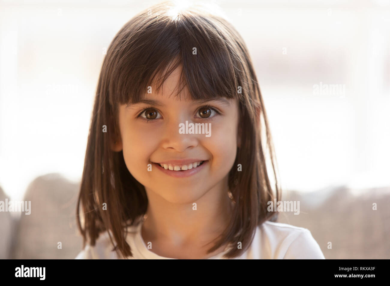 Cute Little Girl sonriendo mirando a la cámara en interiores, headshot retrato Foto de stock