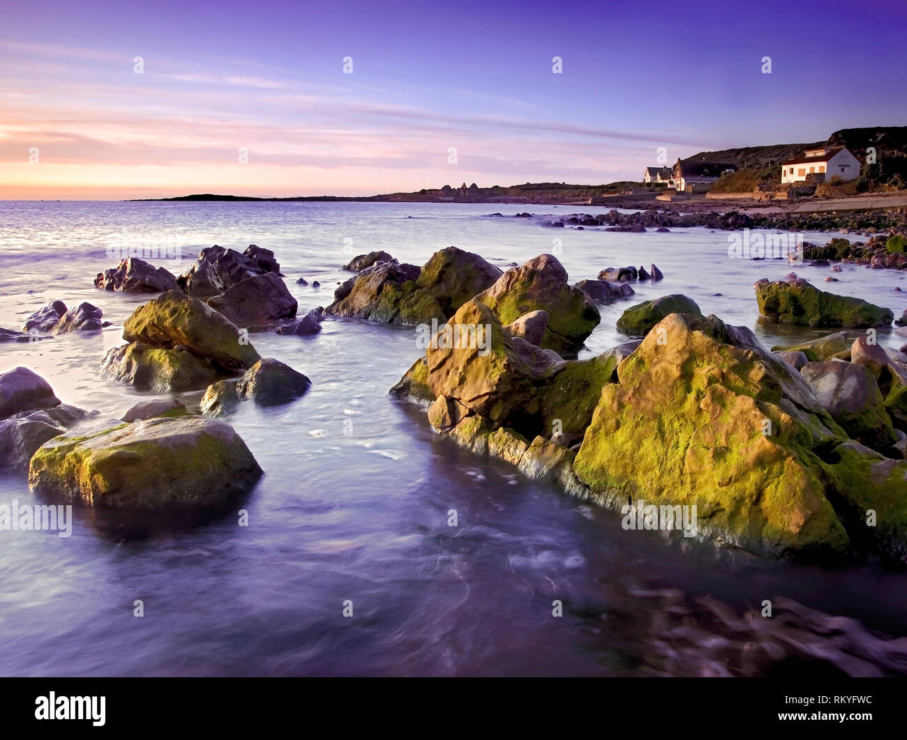 Una vista del amanecer de Port Eynon como sale el sol para iluminar la costa rocosa. Foto de stock