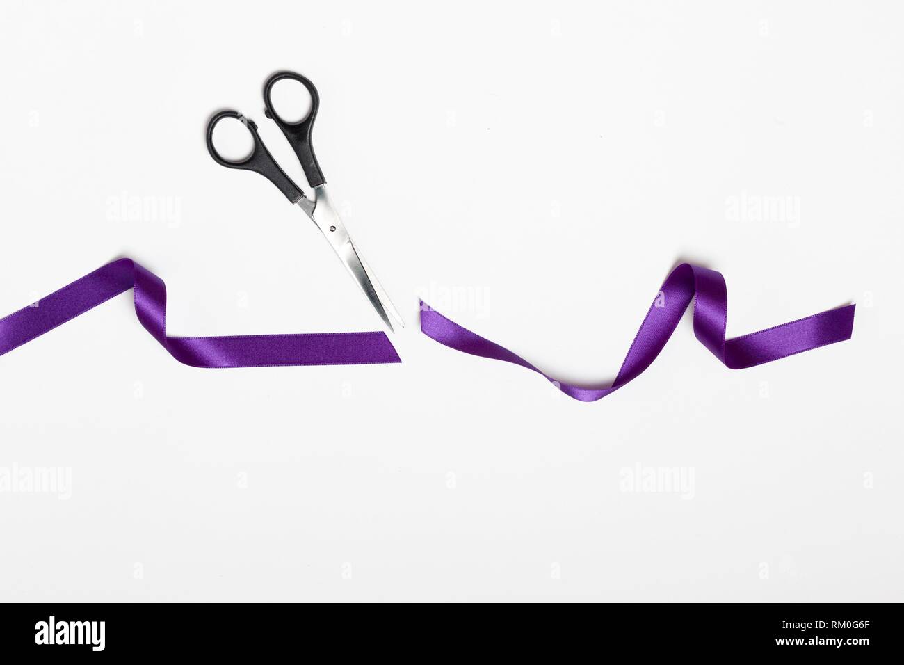 Tijeras de corte de cinta de tela símbolo feminismo violeta sobre fondo blanco. Foto de stock