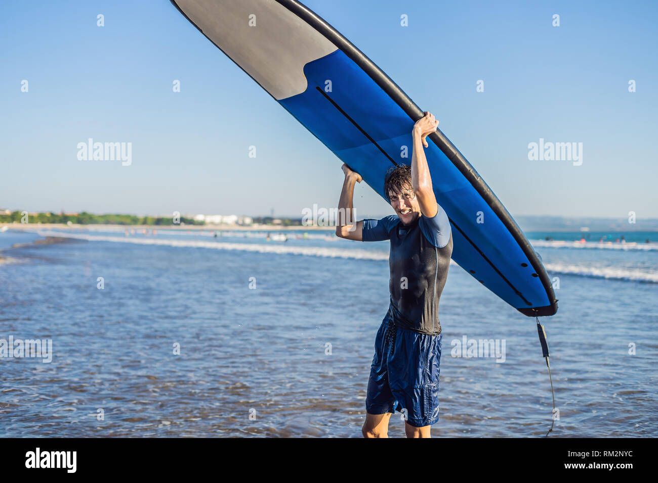 El hombre lleva surf por encima de su cabeza. Cerca de guapo con tablas de surf en la cabeza en la playa. Retrato de hombre con tablas de surf en cabeza y HID Foto de stock