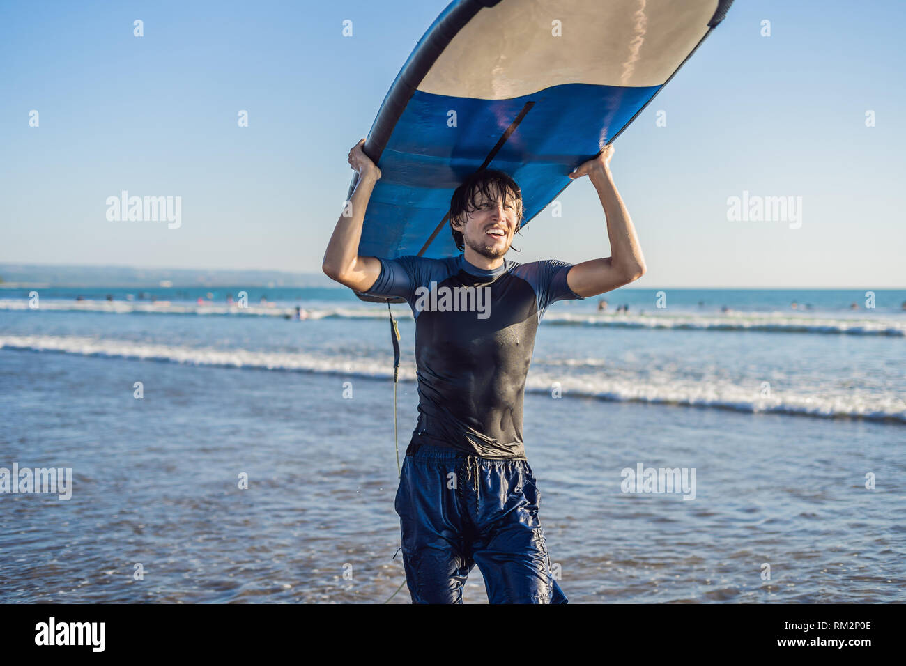 El hombre lleva surf por encima de su cabeza. Cerca de guapo con tablas de surf en la cabeza en la playa. Retrato de hombre con tablas de surf en cabeza y HID Foto de stock