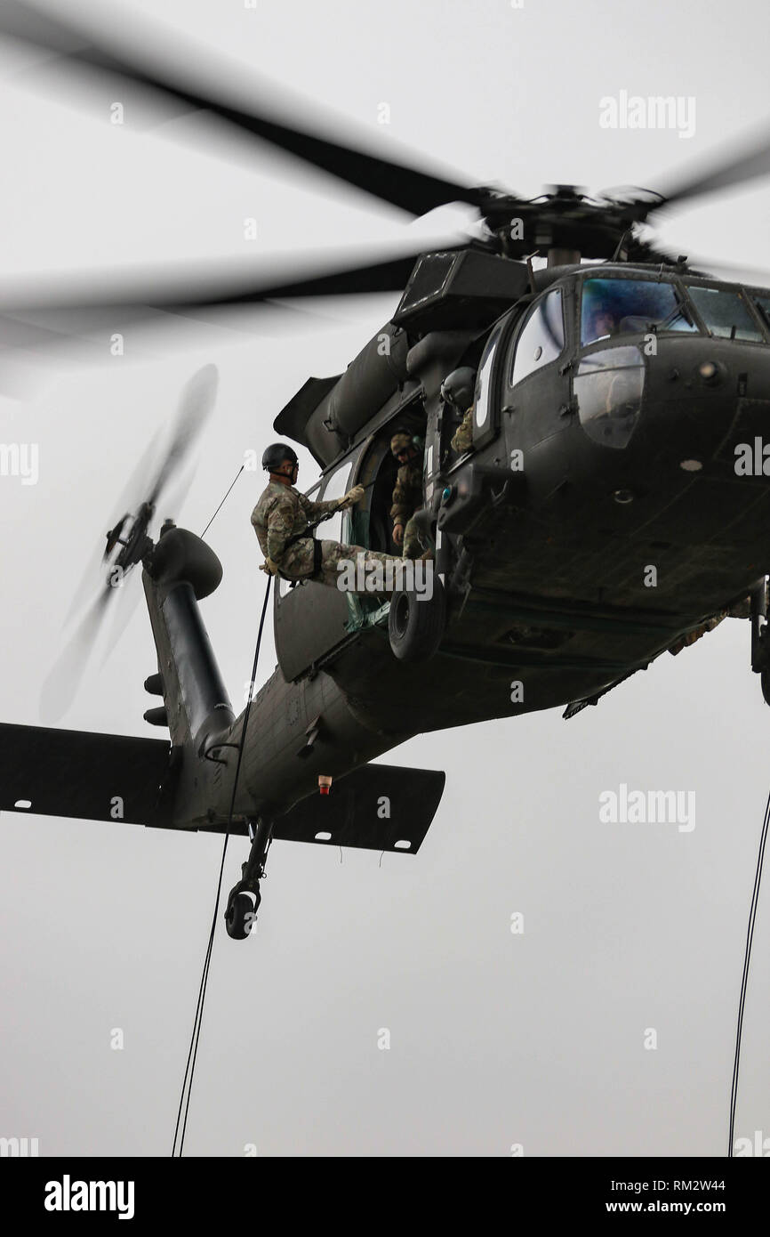Un soldado del Ejército de EE.UU. se prepara para repeler desde un helicóptero Black Hawk UH-60 Cuerda rápido durante la formación del sistema de inserción y extracción en la zona de aterrizaje Udairi, Camp Buehring, Kuwait, el 9 de febrero de 2019. Los instructores de la Guardia Nacional del Ejército Warrior Training Center, en Fort Benning, Georgia, entrenado y cualificado a la tripulación asignada al 1er Batallón del 108º Regimiento de Aviación, la Guardia Nacional del Ejército de Kansas, en preparación para un asalto del aire durante este mes. La foto es borrosa para proteger la seguridad operacional. (Ee.Uu. Foto de la Guardia Nacional del Ejército por el sargento. Emily Finn) Foto de stock