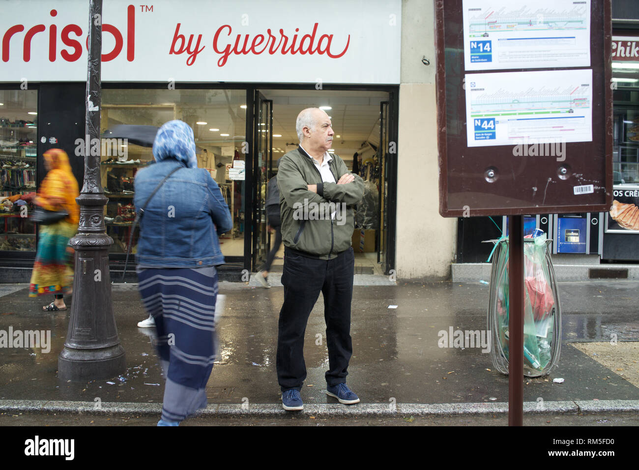 Hombre esperando en la parada del autobús temporal como peatones caminando por el boulevard Barbès, París, Francia Foto de stock