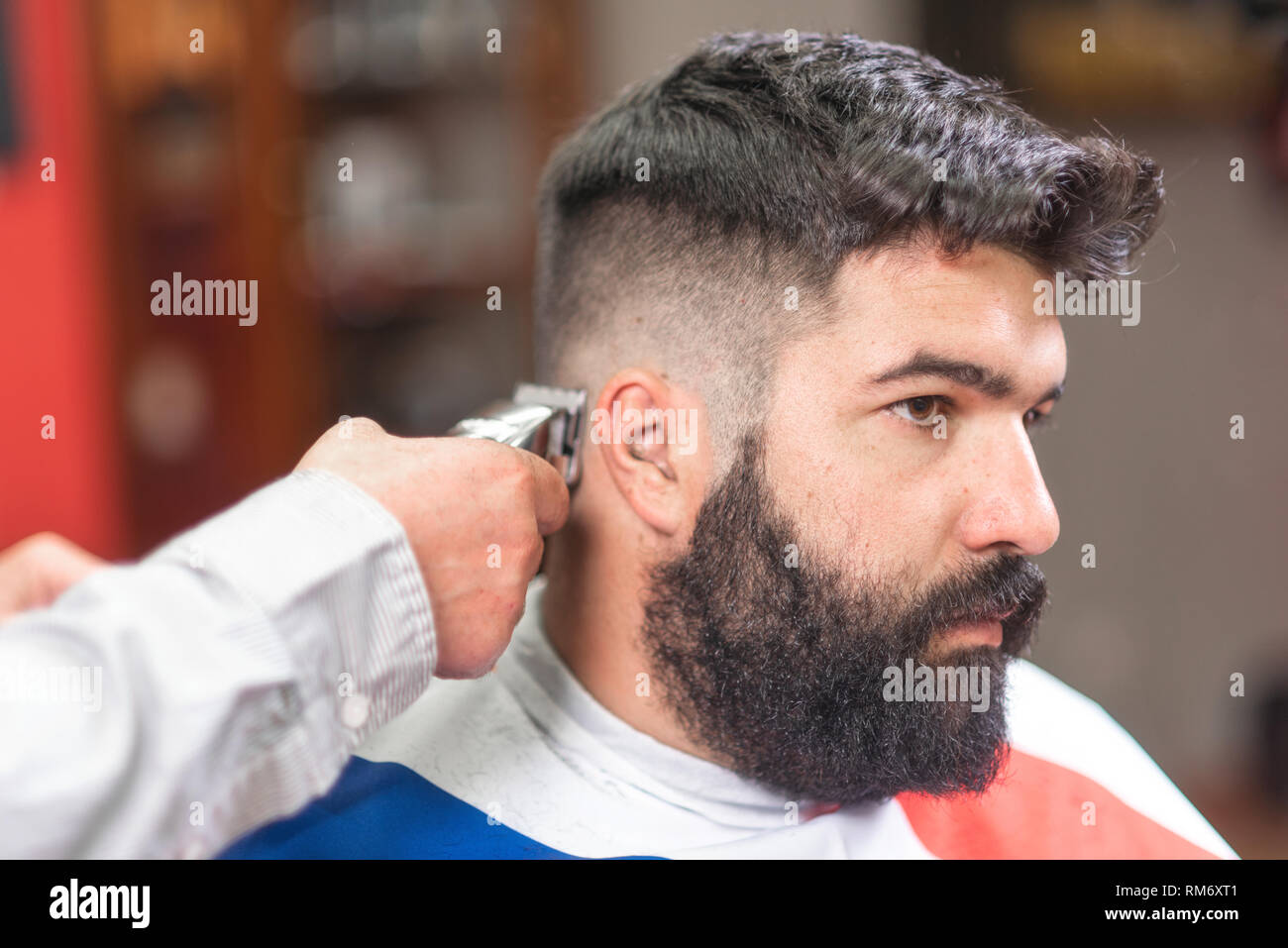Apuesto hombre barbado, obtención de corte de pelo Barber, con recortador  eléctrico en el barbershop Fotografía de stock - Alamy