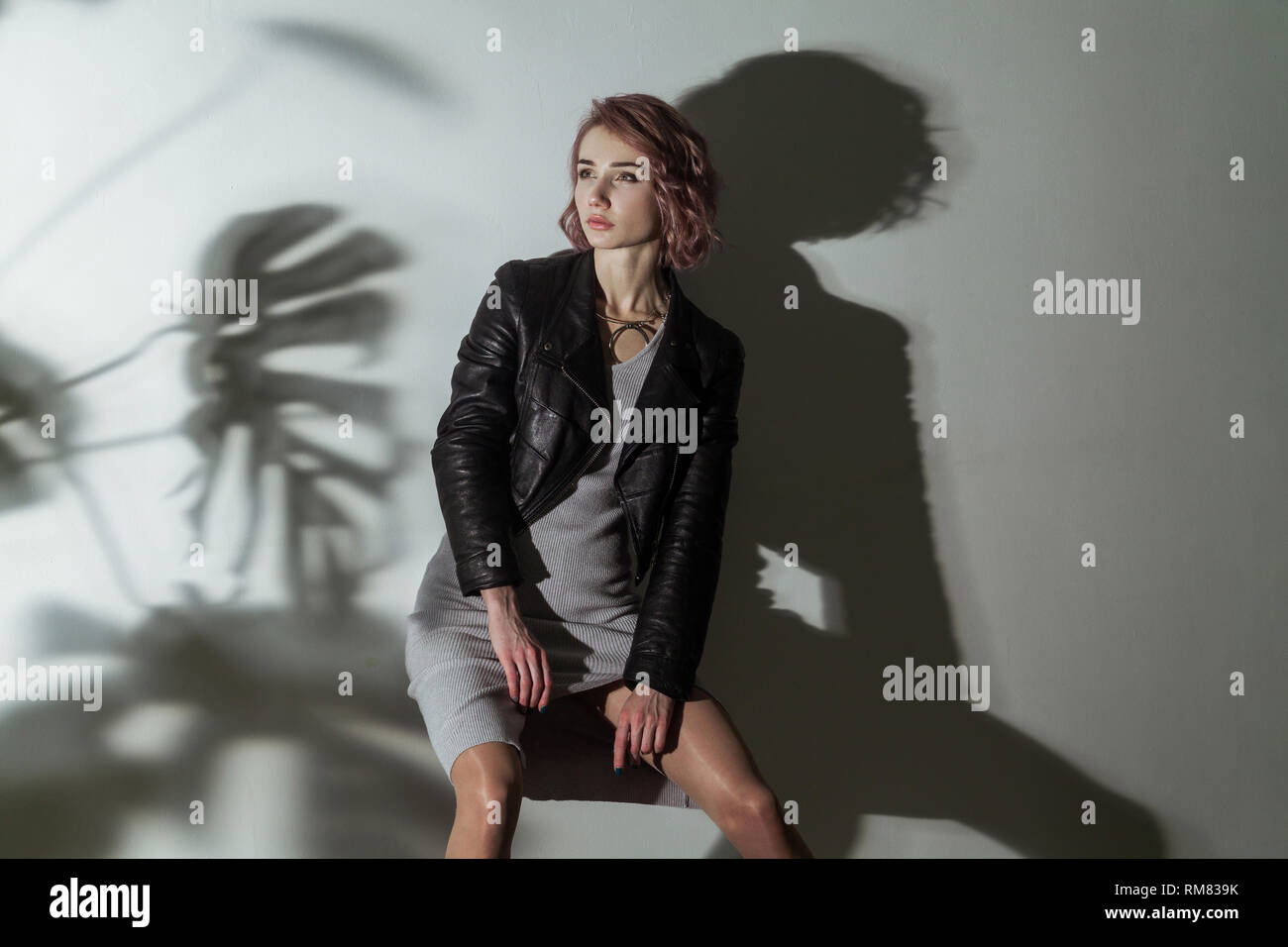 Hermosa mujer con maquillaje y corta el pelo rosa en gris vestido y chaqueta  de cuero negro posando sobre fondo gris con sombra oscura de textura de  hoja pattée Fotografía de stock -