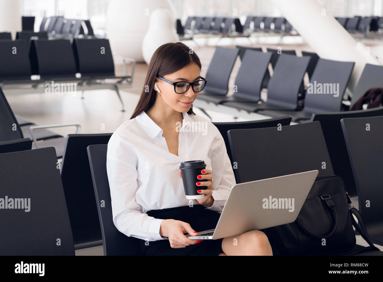 Elegante joven mujer de negocios en la terminal del aeropuerto internacional, trabajando en su ordenador portátil mientras esperando el vuelo Foto de stock