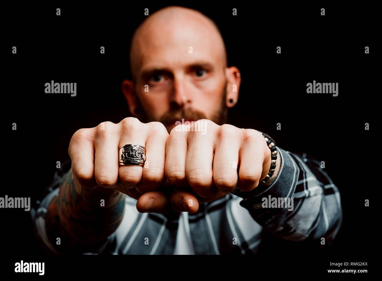 Grave barbudo hipster en camiseta con tatuajes en la mano mostrando los puños con anillo sobre fondo negro Foto de stock
