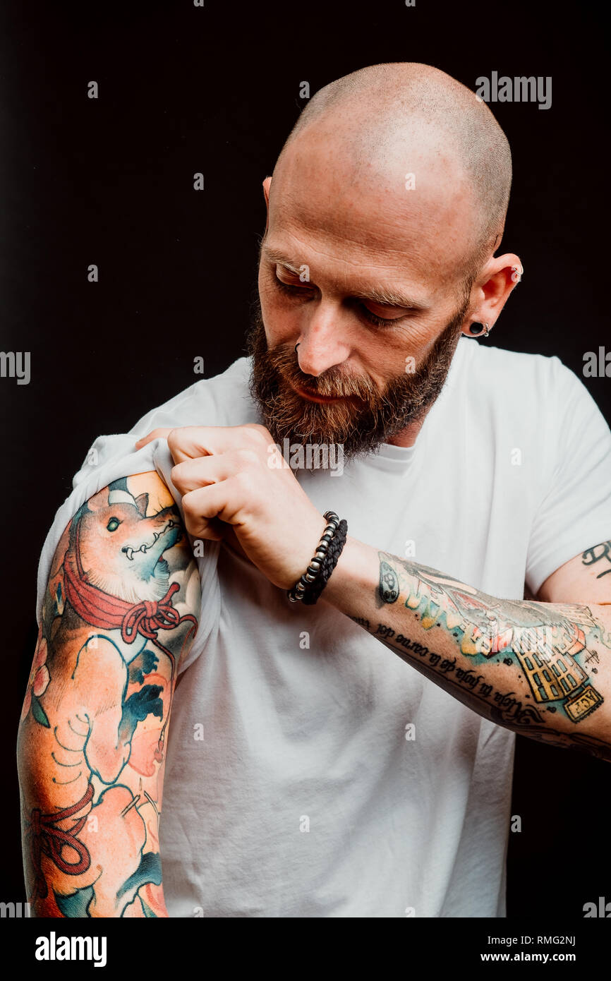 Barba lampiña hipster en t-shirt mostrando tatuajes en manos sobre fondo negro Foto de stock
