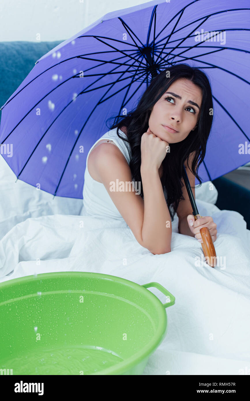 Triste chica con paraguas mirando el agua goteando desde el techo en  dormitorio Fotografía de stock - Alamy