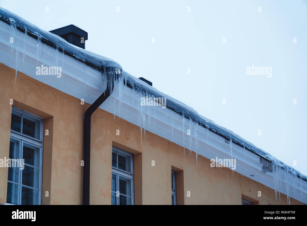 La nieve comienza a derretirse en el tejado de un edificio y colgando a lo largo de la línea del techo en un cálido día de invierno, Helsinki, Finlandia Foto de stock