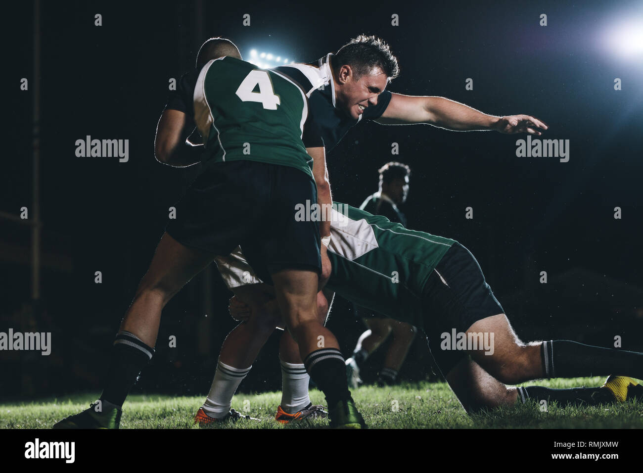 Los jugadores de rugby haciendo un esfuerzo para conseguir la bola del jugador del equipo rival. Los jugadores de rugby que compiten en match bajo luces. Foto de stock