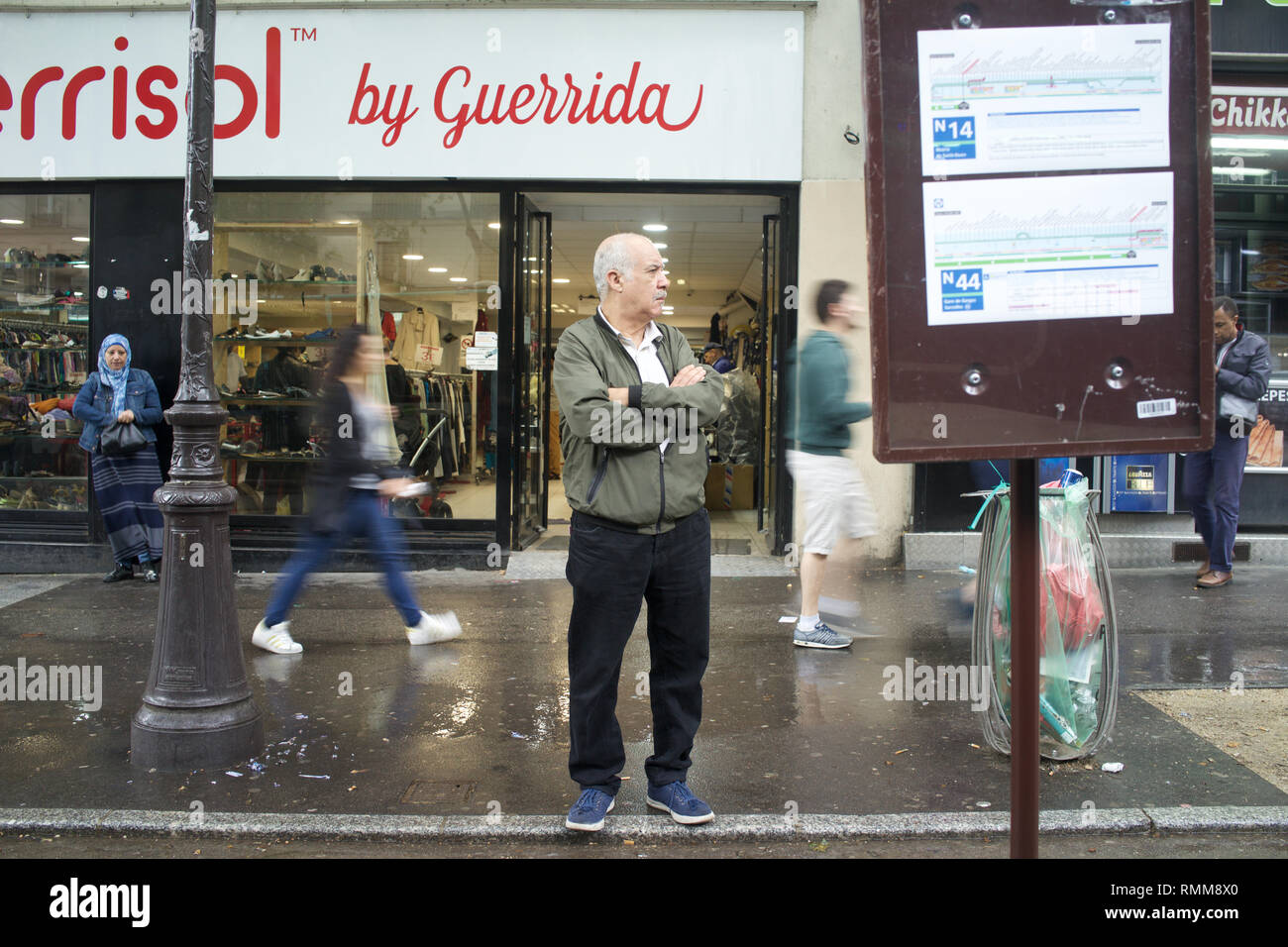 Hombre esperando en la parada del autobús temporal como peatones caminando por el boulevard Barbès, París, Francia Foto de stock