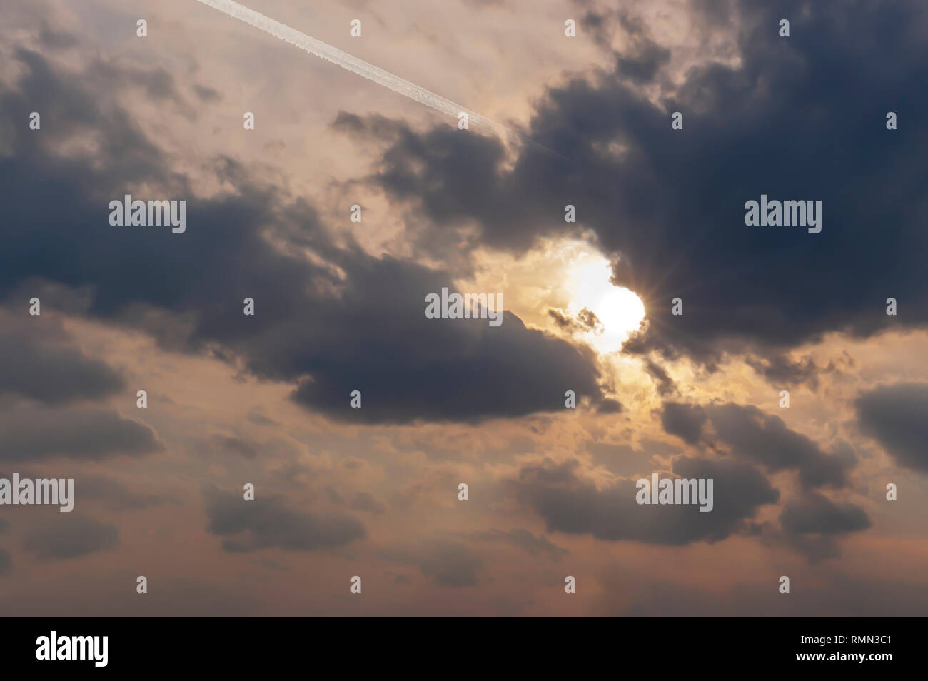 Un avión de pasajeros, dejando una gruesa estelas de condensación, vuela en un banco de estratocúmulos nubes en el cielo. Destello/Buda rayos emanan de un Sol parcialmente oculto Foto de stock